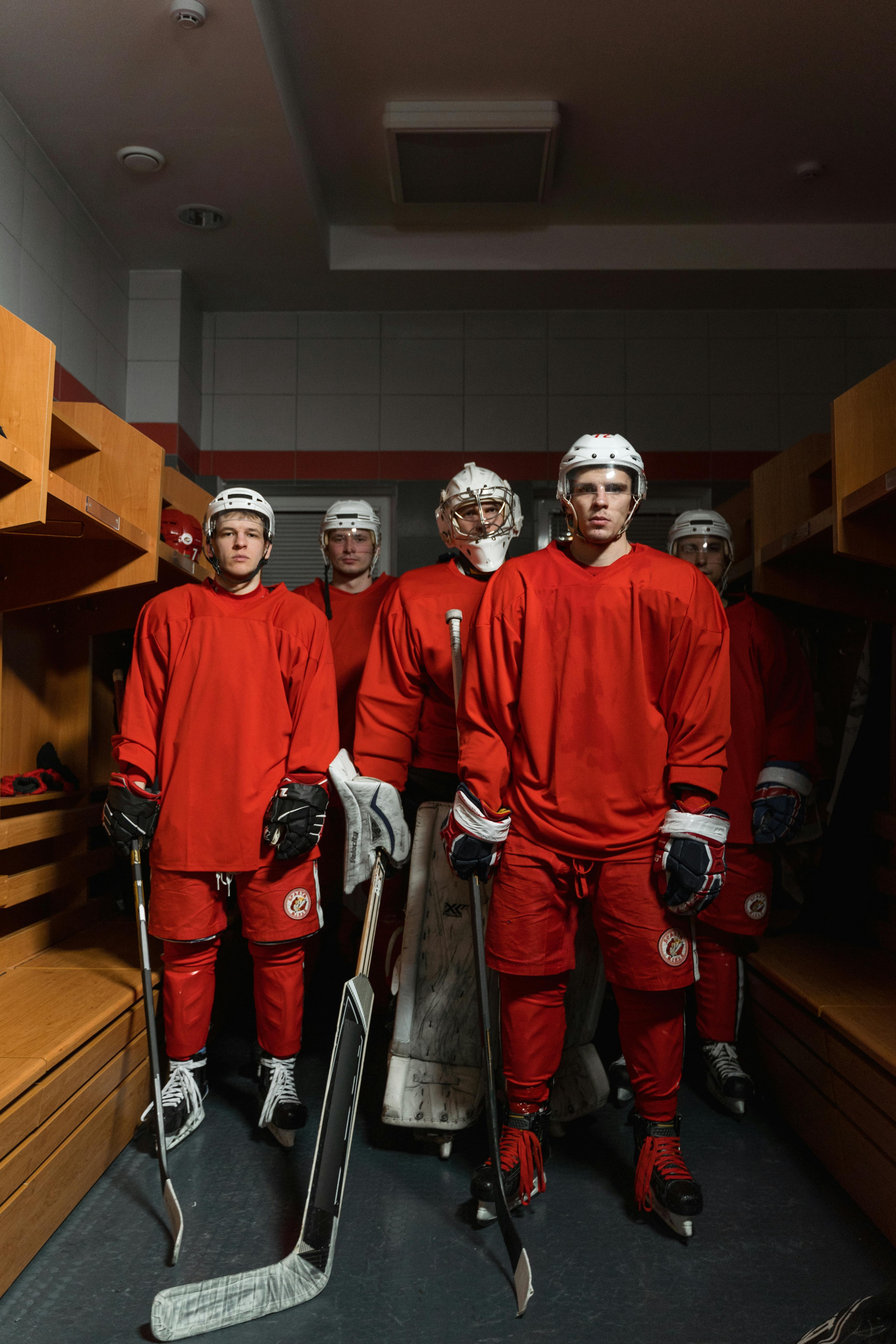 Team of hockey players in red uniforms standing in locker room with gear.