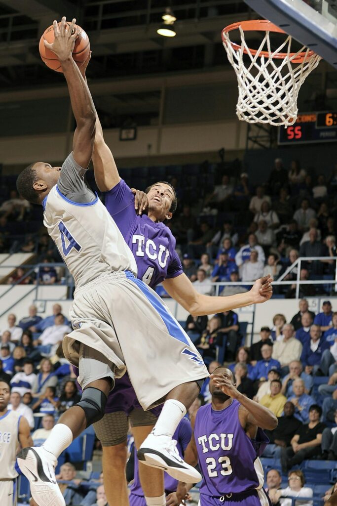 Players from two college teams compete fiercely for a basket during a lively game.