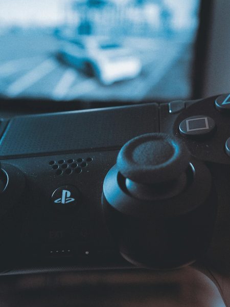 A hand holding a wireless game controller in front of a blurry screen, capturing the gaming experience.