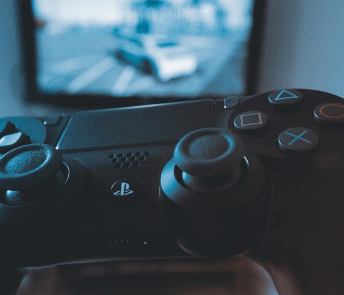 A hand holding a wireless game controller in front of a blurry screen, capturing the gaming experience.