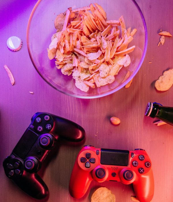 Top view of a bowl of chips surrounded by gaming controllers on a wooden surface.