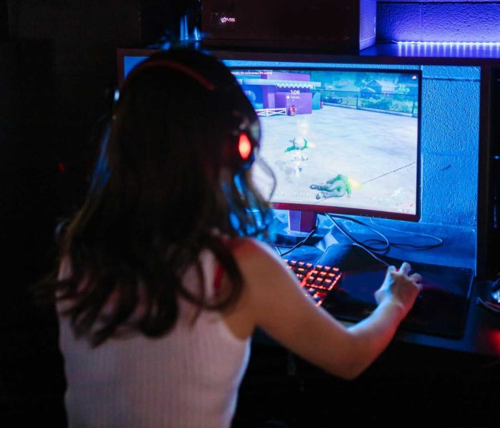 Female gamer focused on playing a competitive online game with RGB keyboard and headphones.
