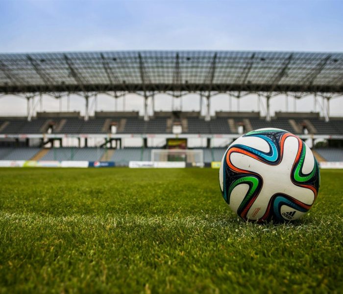 Close-up of a soccer ball on a lush grass field with an empty stadium in the background.